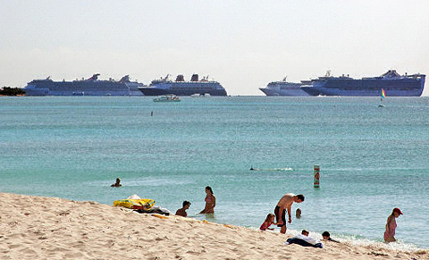 Cruise ships moor off George Town in the background as beachgoers enjoy Seven Mile Beach.