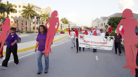 Deputy Governor Franz Manderson, center, joins activists carrying red silhouettes representing victims of domestic violence as they march through George Town on Monday evening