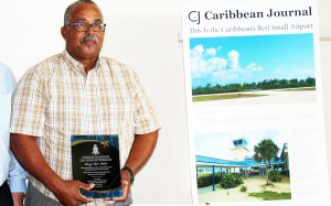 Bud Walton poses in front of the Caribbean Journal article recognizing the Brac’s airport as the best small airport in the region. - PHOTOs: JAMES WHITTAKER