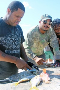 Bradley McLaughlin, Hugh Bush and Kevin Levy clean fish on the Coe Wood Public Beach in Bodden Town. - Photos: Jewel Levy