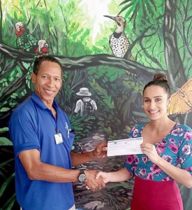 Curator of terrestrial exhibits and education programs of the Cayman Turtle Farm, Geddes Hislop, hands over the check to Danielle Watler, marketing manager at the Cayman Islands National Trust.