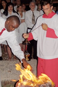 O’Neil Miller retrieves a piece of charcoal from the fire at St. Ignatius Catholic Church. The acolyte holds an incensorium in which the charchoal will be placed. Incense will be added for use later in the service. - Photo: CAROL WINKER