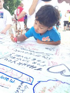 Four-year-old Jordan Johnson writes his thank-you message on Save the Cove picnic tables.