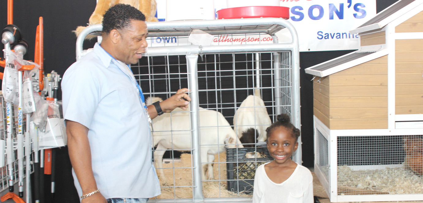 Young Naima Myles learns about goats and chickens from Glen Roy Clarke of A.L. Thompson's. The store's booth highlighted goats, chickens and tools at the MarketPlace Outdoor Living Expo held at the ARC at Camana Bay Thursday. - PHOTOS: JEWEL LEVY