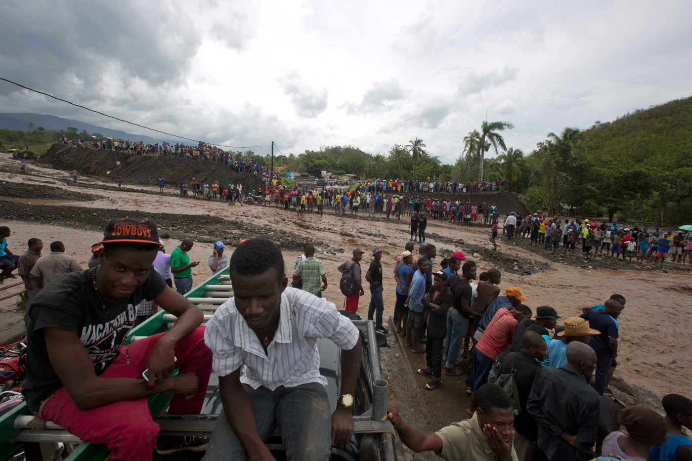 People watch from both sides of the La Digue river as water roars past where the Petit Goave bridge once stood, destroyed by Hurricane Matthew, in Petit Goave, Haiti, Wednesday, Oct. 5. - Photo: AP