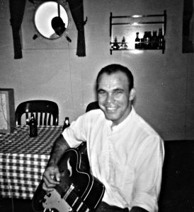 A young Arlin Tatum strumming his guitar on board a ship.