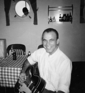 Capt. Arlin Tatum playing the guitar while at sea circa 1959.