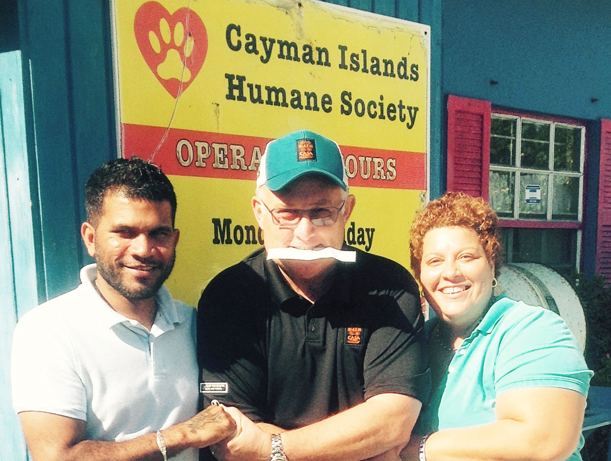 Max Hillier, co-owner of Casa 43, delivers, in his mouth, a check to Jason Jairam and Letty Blanco of the Humane Society.