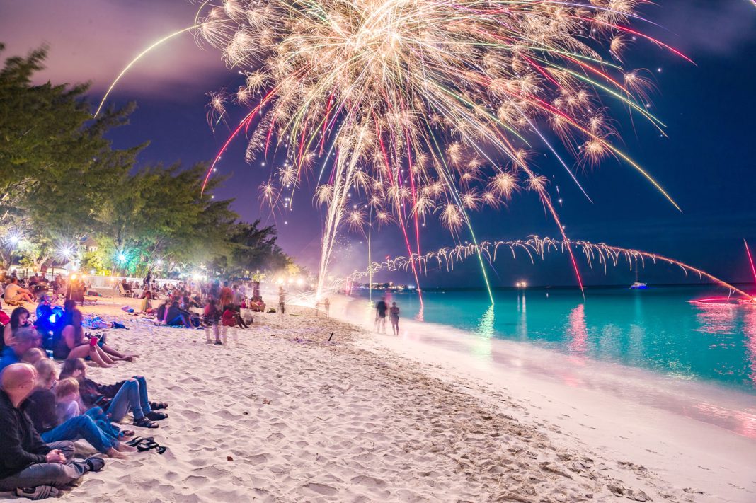 Residents and visitors gaze up at fireworks launched just before midnight on New Year’s Eve along Grand Cayman’s Seven Mile Beach. - Photo: Taneos Ramsay