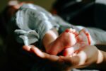 Proposed parental leave changes do not go far enough, says working group A person holds a baby's feet. - Photo: Omar Lopez, Unsplash