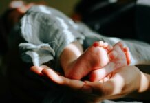 Proposed parental leave changes do not go far enough, says working group A person holds a baby's feet. - Photo: Omar Lopez, Unsplash