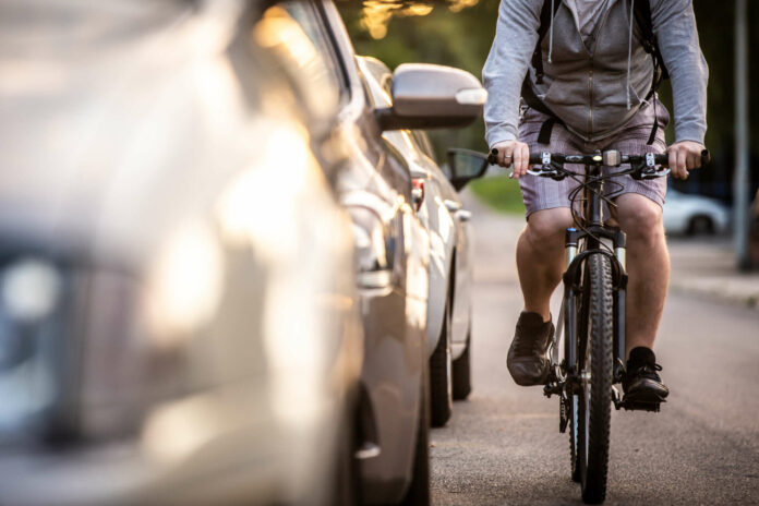 An unidentified man riding a bicycle passing cars on the road in the traffic. A cyclist overtaking cars with high speed.